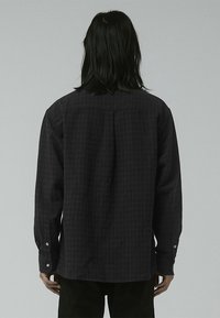 Black plaid long-sleeve shirt with a relaxed fit, button cuffs, and visible back seam details. Made of a textured fabric.
