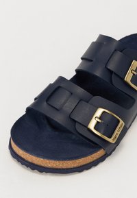Mørkeblå sandaler med to justerbare stropper, guldtonede spænder og en korksål. Blødt tekstureret indlæg for komfort.