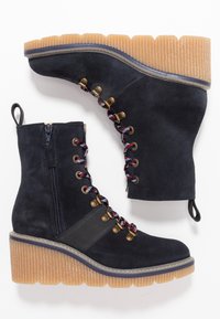 Botas de tobillo de ante azul marino con una suela de goma gruesa y con estrías. Presenta cordones coloridos, ojales en tono dorado y una cremallera lateral para facilitar su uso.