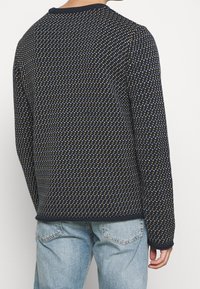 Mörkblå tröja med strukturerad stickning, prydd med ett geometriskt mönster av små vita och senapsfärgade former. Ribbad halsringning och ärmslut.