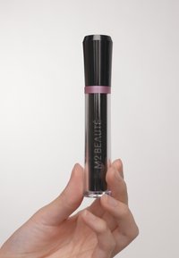 Contenedor cilíndrico transparente con tapa negra y acento rosa. La etiqueta dice "M2 BEAUTE". Contiene un producto con líquido de color oscuro en su interior.