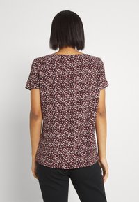 Camiseta floral color burdeos de manga corta, con un pequeño patrón de flores multicolores. Tejido suave, con un corte holgado y escote redondeado.