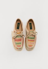 Chaussures décontractées beiges avec un textile tissé multicolore sur le dessus, présentant un bout arrondi, des détails en lacets, et une semelle légère.