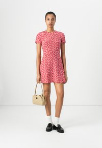 Robe florale rouge à manches courtes, corsage ajusté, jupe évasée, associée à un sac à main beige et des mocassins noirs. Chaussettes blanches visibles.