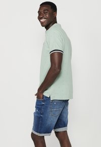 Polo verde chiaro con piccoli motivi, dettagli in bianco e nero sulle maniche, abbinato a pantaloni corti in denim con orli arrotolati.