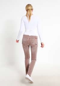 Jeans de corte ajustado en un tono rosa claro, con un acabado ligeramente texturizado, que cuentan con dos bolsillos traseros y detalles de costura sutiles. Combinados con una blusa de manga larga blanca.
