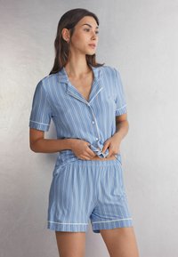 Blauwgestreept kort pyjama-set gemaakt van zachte stof. De top heeft een knoopsluiting aan de voorkant en korte mouwen, terwijl de shorts een elastische tailleband hebben.