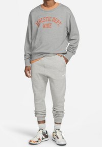 Šedá mikina s nápisem "ATHLETIC DEPT. NIKE" v oranžové barvě, zkombinovaná se šedými tepláky a multibarevnými teniskami se vzorem. Bavlněný materiál.