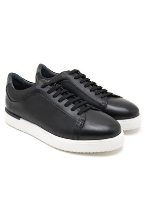 Baskets en cuir noir au design minimaliste, avec une semelle en caoutchouc blanc, un bout rond et des lacets noirs. Texture lisse, lignes épurées.