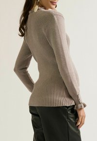 Lange mouwen geribbeld sweater in licht taupe, met een gerimpelde zoom, knoopmanchetten en een getailleerd silhouette. Soepele textuur met verticale lijnen.
