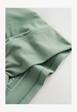 Zöld aktív viselet, puha, rugalmas anyagból. Simító textúrával, lapos varratokkal és a "NEXT" márkázású címkével a alsó szélén.