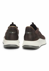 Ein Paar dunkelbraune Sportschuhe mit weißen Sohlen, von hinten betrachtet, die Fersenlaschen und die strukturierten Ränder der Außensohle zeigen.