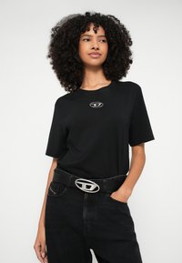 Μαύρο βαμβακερό t-shirt με ασημένιο λογότυπο στο στήθος, σε συνδυασμό με μαύρο τζιν ψηλόμεσο και μαύρη ζώνη με ασημένια αγκράφα.