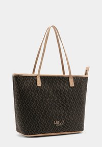 Tragetasche aus dunkelbraunem synthetischem Material mit wiederholtem Logo-Muster, beigen Griffen und einem goldfarbenen Markennamen-Detail.