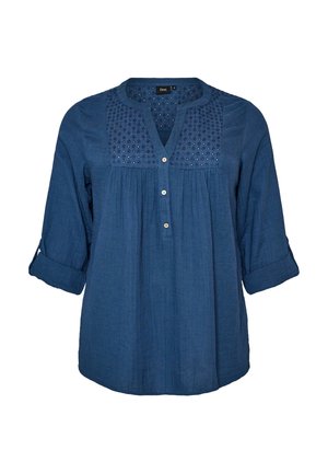 Blue long-sleeve blouse with rolled cuffs, buttoned front placket, and decorative cutout panel with small holes on the chest area.