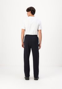 Marineblaue Sweatpants mit elastischem Bund, gerade geschnitten, kombiniert mit einem schlichten weißen T-Shirt, vor einem weißen Hintergrund präsentiert.