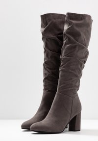 Stivali grigi morbidi al ginocchio in suede, con tacco spesso e una texture liscia, arricchiti da dettagli arricciati nella parte superiore.