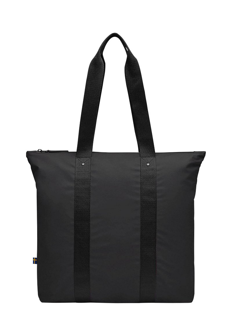 Svart tote bag med en glatt, matt finish, utstyrt med to brede tekstilhåndtak og glidelås på toppen. Lite logo-detall på siden.
