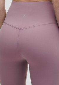 Magasan derekú levendula színű sport leggings, sima, rugalmas anyagból készült, megerősített varrással és logó részletekkel a hátsó részen.