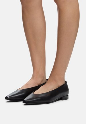 Chaussures plates en cuir noir avec un bout pointu, un petit talon et un design de découpe subtil, présentant une texture lisse et un style minimaliste.