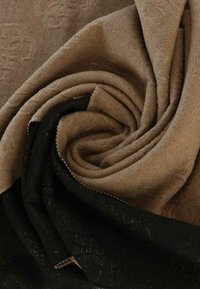 Tessuto marrone e nero textured drappeggiato a spirale, evidenziando i motivi intrecciati e i colori contrastanti, con cuciture visibili lungo i bordi.
