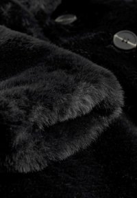Gros plan sur un tissu de pelage noir doux avec deux boutons brillants partiellement visibles en arrière-plan.