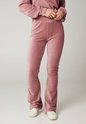 Pantalones acampanados de pana rosa con una textura suave, que presentan una cintura alta y un diseño ajustado. Llevados con zapatillas blancas.