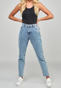 Džíny s vysokým pasem v světle modré barvě, volný střih, pět kapes a zapínání na knoflík. Doplněno černým žebrovaným tílkem a bílými teniskami.