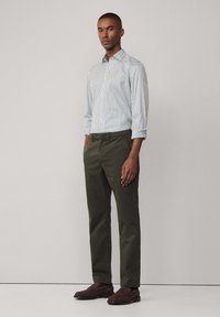 Camicia a maniche lunghe a righe in bianco e blu, abbinata a pantaloni verde scuro e scarpe slip-on marrone scuro, con un fit pulito e rilassato.