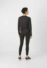 Musta pitkähiha-paita, jossa on pyöreä pääntie, yhdistetty mustiin legginsseihin ja urheilukenkiin, joissa on harmaa ja violetti yksityiskohta. Sujuva pinta.