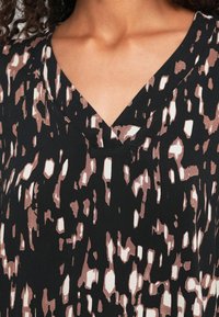 Sort bluse med V-udskæring, prydet med et abstrakt mønster i nuancer af beige og hvid, samt en let og glat stoftekstur.