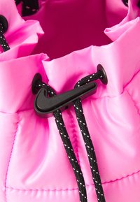 Cinghia nera a forma di logo Nike Swoosh che tiene bloccati i cordini bianco e nero su un tessuto trapuntato di un brillante rosa.