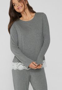Top de manga larga gris hecho de una tela suave con un ribete de encaje blanco en la parte inferior. Combinado con pantalones de pijama grises a juego.