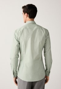 Lysegrøn skjorte med knapper, klassisk krave, lange ærmer og afrundet kant. Glat stof med en subtil glans og manchetter.