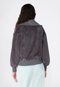 Pull en peluche gris avec un col et des poignets côtelés, présentant une coupe décontractée et des manches bouffantes. Texture douce, design uni sans motifs.