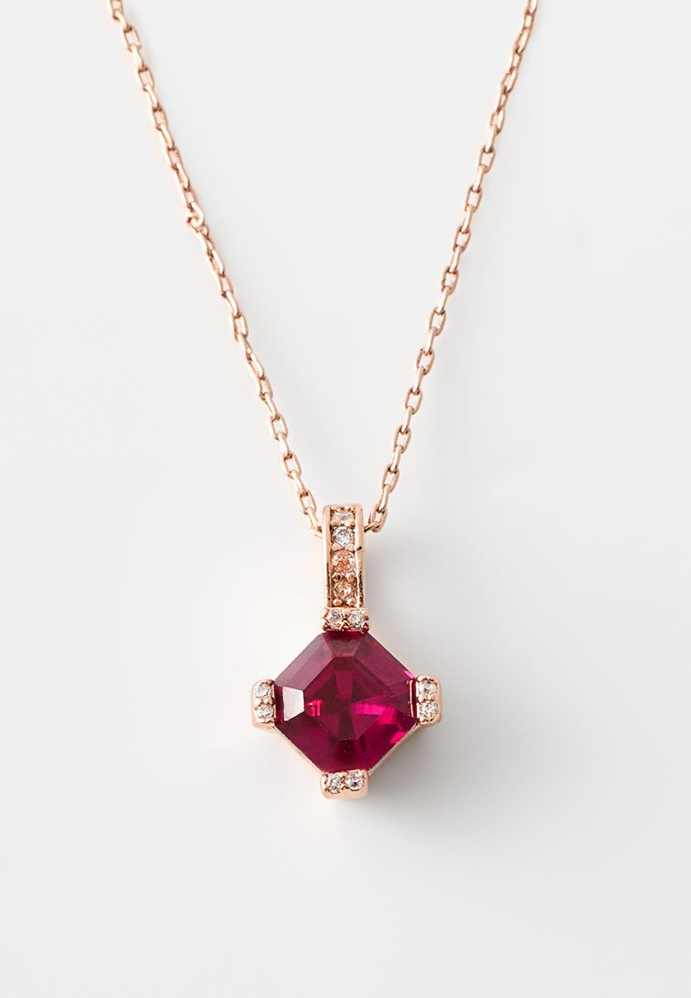 Collana in oro rosa con pendente di rubino sfaccettato, circondato da piccole pietre trasparenti; la catena presenta un motivo a maglie.