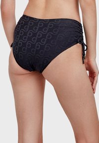 Bas de maillot de bain noir avec un motif texturé présentant des courbes abstraites. Liens latéraux ajustables pour un meilleur ajustement. Tissu lisse et extensible.