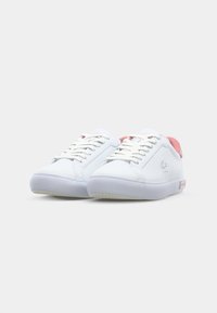 White sneakers with a smooth leather upper, pink accents on the heel and tongue, and a translucent rubber outsole. Features laces and logo.