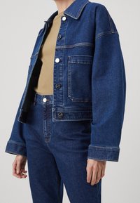 Tummansininen farkkutakki rento istuvuus, suuret etutaskut, hopeanväriset koristeet ja kontrastivaateiset ompeleet. Yhdistetty vastaaviin farkkuihin.