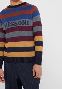 Gestreepte gebreide trui met gedurfde kleuren: rood, blauw, grijs, bordeauxrood en geel. Gestructureerde stof met het "MISSoni"-logo op de borst.