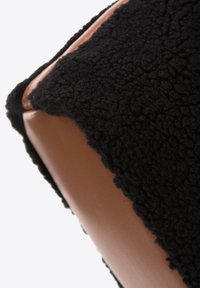 Tissu noir texturé combiné avec du cuir marron lisse, formant une forme rectangulaire avec des coutures proéminentes et une surface douce.
