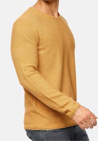Suéter de cuello redondo de manga larga en amarillo dorado, con textura de punto, que presenta motas sutiles, con puños y dobladillo acanalados.
