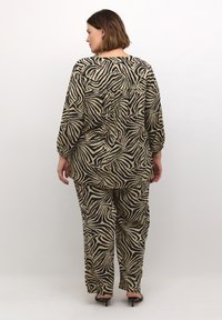 Zebra vzorovaný outfit v béžovej a čiernej farbe; voľný top s dlhými rukávmi a zodpovedajúce nohavice; hladká textília s jemnou textúrou.