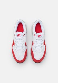 Sneaker in rete bianco e suede rosso con design a lacci, collo imbottito e suola nera. Presenta il logo Nike sulla linguetta e sul lato.