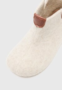 Crème-kleurige vilten slof met een ronde neus en een textuurafwerking, met een bruine leren accent bij de hiel voor gemakkelijke draagbaarheid.