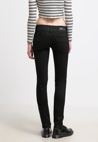 Černé skinny džíny s vysokým pasem, zadními kapsami a hladkým povrchem. Nosené s krátkým pruhovaným topem, který má minimalistický design.