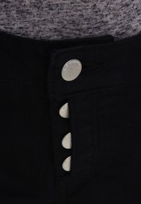 Lähikuva mustista housuista, joissa on neliä näkyvää hopeista nappia ja harmaata kangasta vyötäröllä.