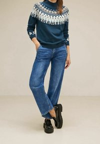 Stickad marinblå tröja med vita geometriska mönster; matchad med ljusblå vida jeans och svarta plattformsskor. Slät textur överlag.