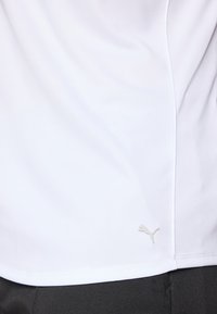 Hvit idretts skjorte laget av glatt stoff, med en grå Puma-logo nederst til venstre, med en litt tettsittende design og subtile sømdetaljer.