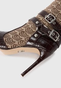 Stivale marrone alla coccodrillo con tomaia in tessuto marrone texturizzato, dotato di fibbie argentate e tacco a stiletto appuntito.